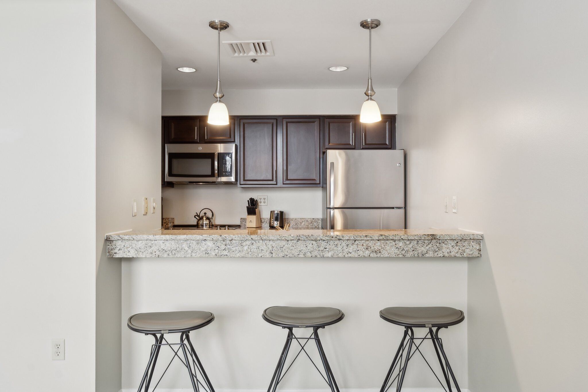 A modern kitchen with granite countertops, stainless steel appliances, and bar stools.