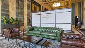 A lobby with a green leather sofa, brown leather armchairs, a wooden coffee table, and a large white sign reading "THE PENNSYLVANIAN."