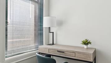 A modern desk with a lamp and a small plant, positioned next to a window with blinds.