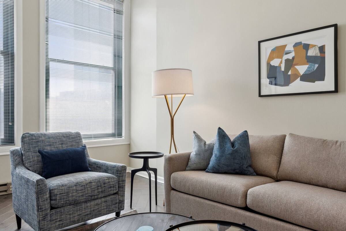 Una sala de estar con un sillón gris, un sofá beige y una lámpara de pie.