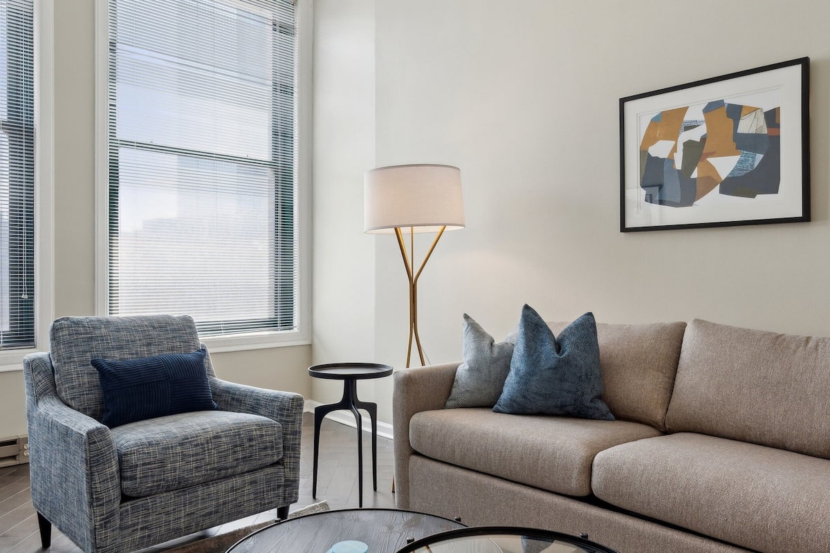A living room with a grey armchair, a beige sofa, and a floor lamp.
