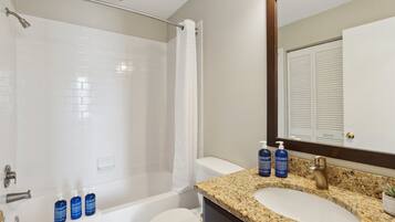 Une salle de bain avec une baignoire, des toilettes et un lavabo. On peut voir trois bouteilles de savon liquide bleu sur le comptoir.