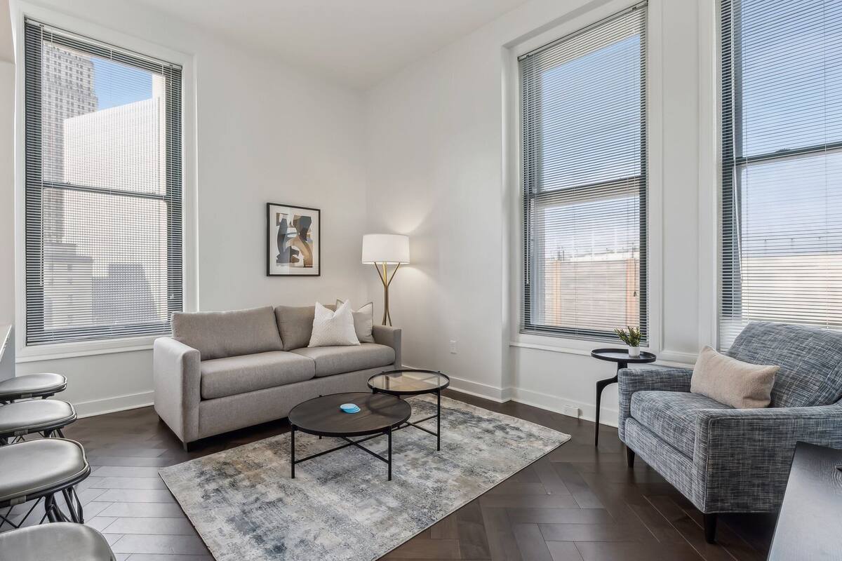 Una sala de estar moderna con un sofá gris, una mesita redonda y un sillón gris.