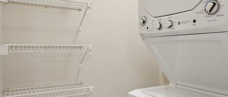 A laundry area with a front-loading washing machine and four wire shelves for hanging clothes.