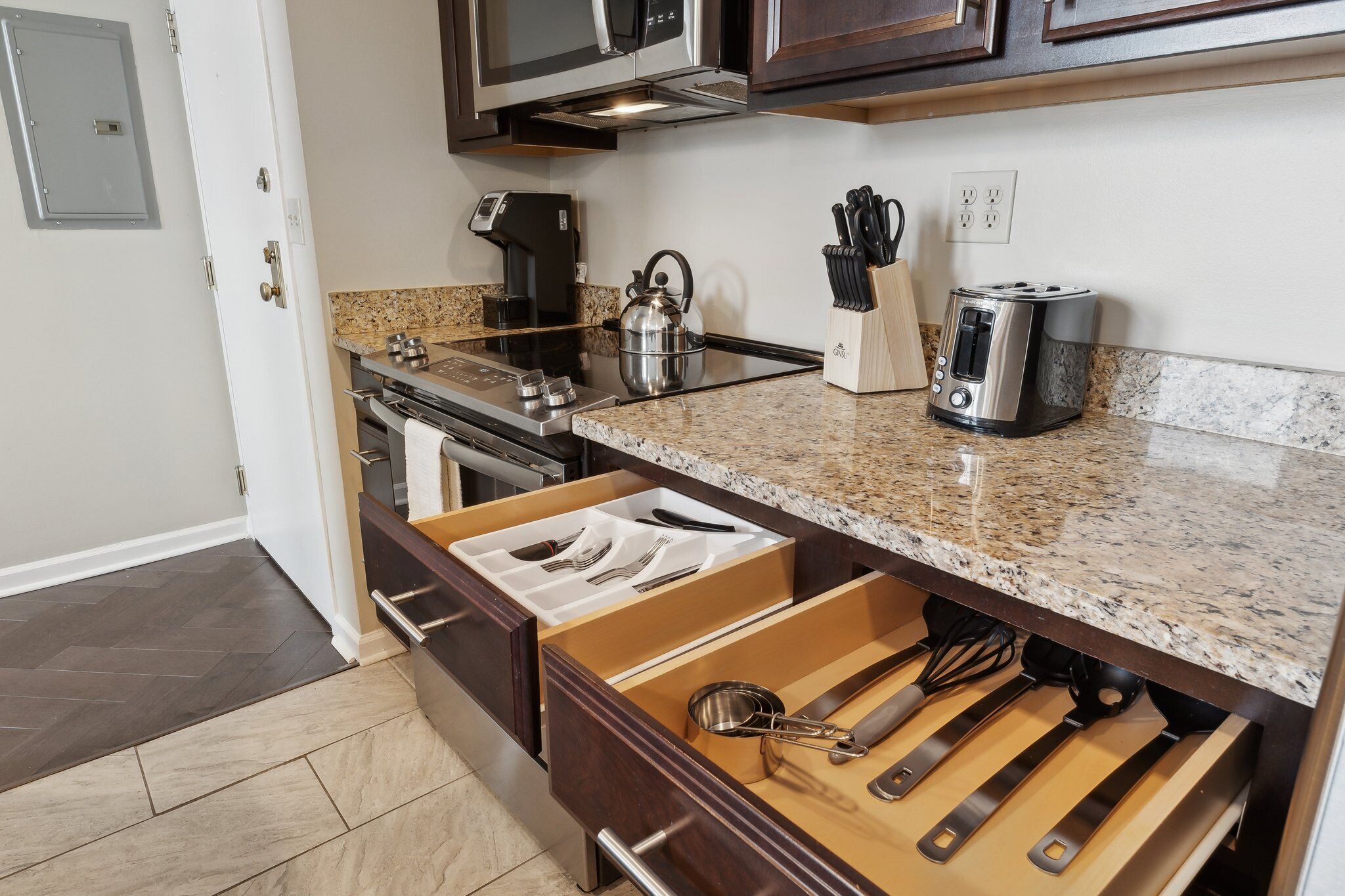A kitchen with a granite countertop, stainless steel appliances, and a drawer organizer with utensils.