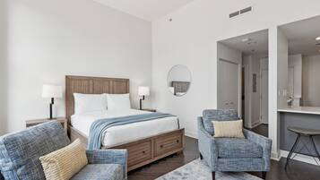 Une chambre à coucher moderne avec un lit en bois, deux fauteuils, un petit bureau et un miroir rond accroché au mur.