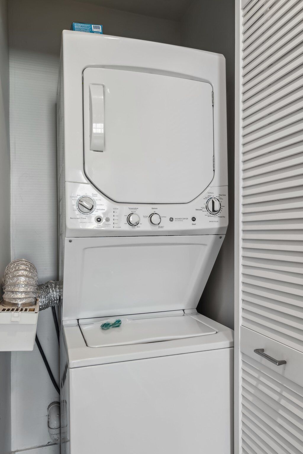 Een was- en droogcombinatie met bedieningspanelen, een zeepdispenser en een opbergruimte met een handvat.