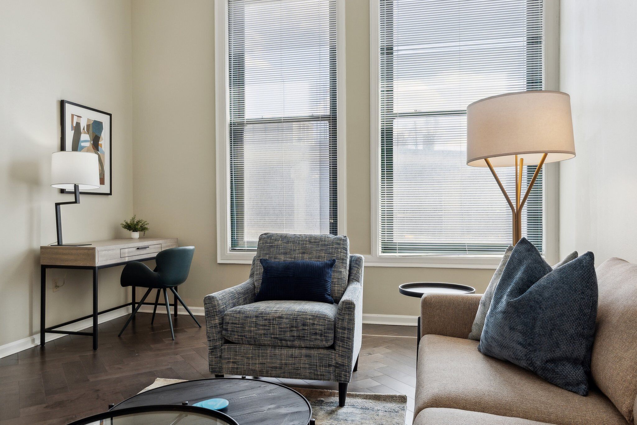 Una sala de estar moderna con un sillón gris, un sofá beige, un escritorio con una silla y una lámpara de pie.