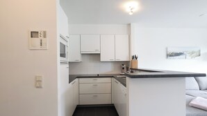 A compact kitchen with white cabinets, a microwave, and a sink. There is a small countertop and a painting on the wall. - Apartment in Oostduinkerke Near the Coast (Koksijde)