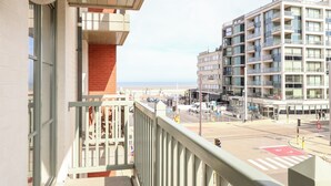 A balcony with a view of a multi-story building, a street with vehicles, and a pedestrian crossing. - Apartment in Oostduinkerke Near the Coast (Koksijde)