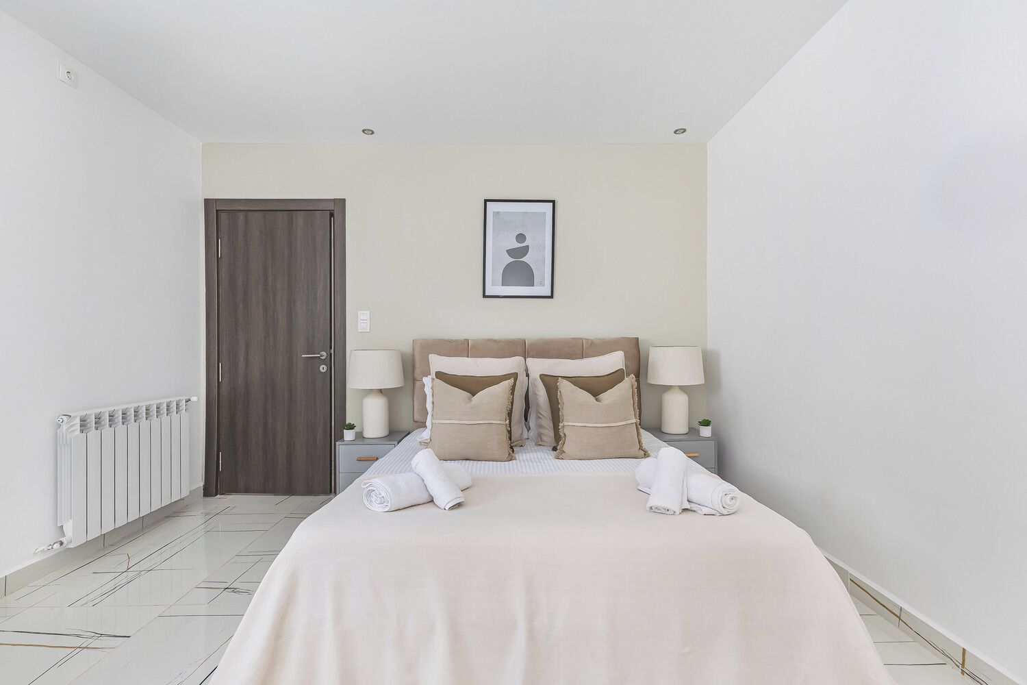 A hotel room with a bed, two bedside tables, a door, a radiator, and a framed picture on the wall.