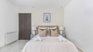 A hotel room with a bed, two bedside tables, a door, a radiator, and a framed picture on the wall.