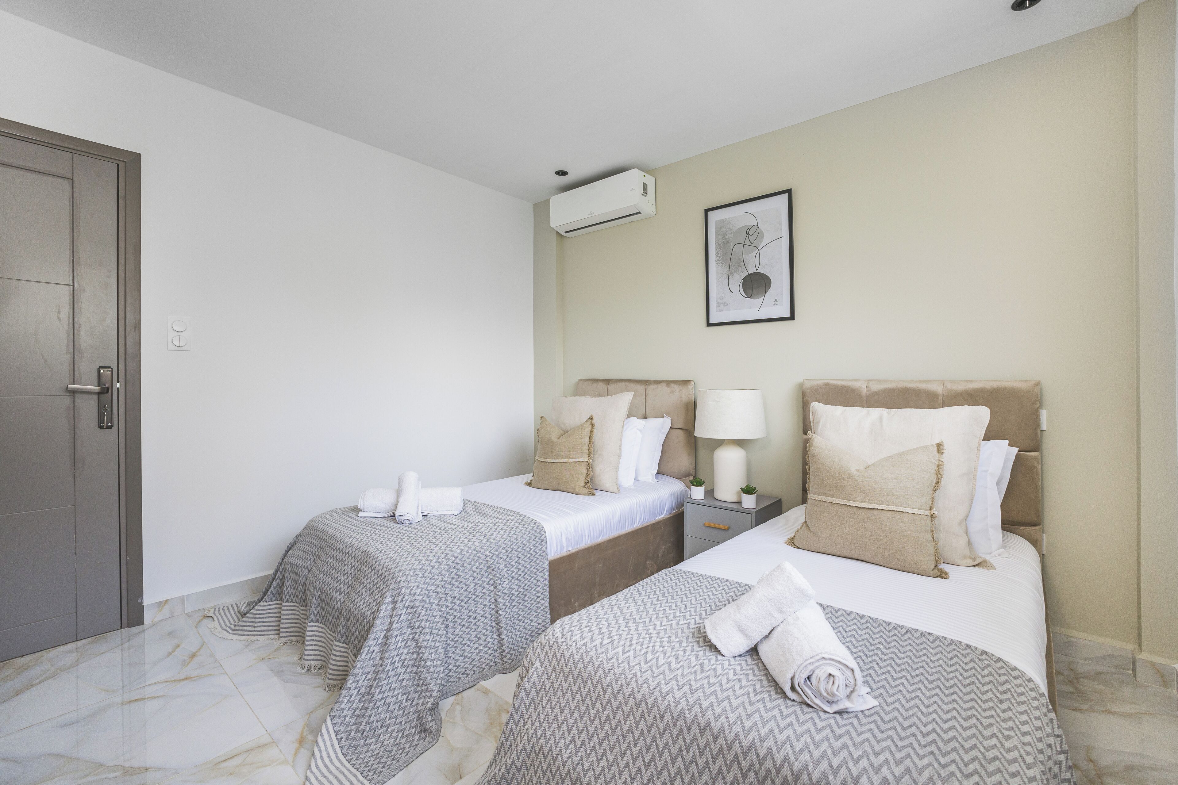 A hotel room with two beds, a door, an air conditioning unit, a framed picture on the wall, and a marble floor.