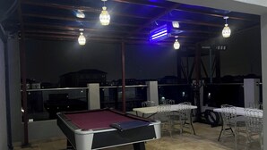 A pool table in a dimly lit room with tables and chairs, a view of buildings outside, and a balcony railing. - Bamgbose Apartments - Sleeps 2 - Parking - Wifi (Lagos)