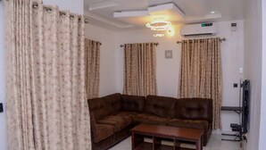 A living room with a brown leather sofa, a wooden coffee table, and beige curtains. - Bamgbose Apartments - Sleeps 2 - Parking - Wifi (Lagos)