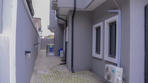 A narrow alleyway with a paved path, a white air conditioning unit, and a blue trash bin. - Bamgbose Apartments - Sleeps 2 - Parking - Wifi (Lagos)