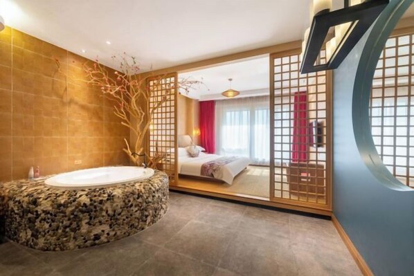 A modern bathroom with a stone bathtub, a wooden partition, and a bed visible through a sliding door.