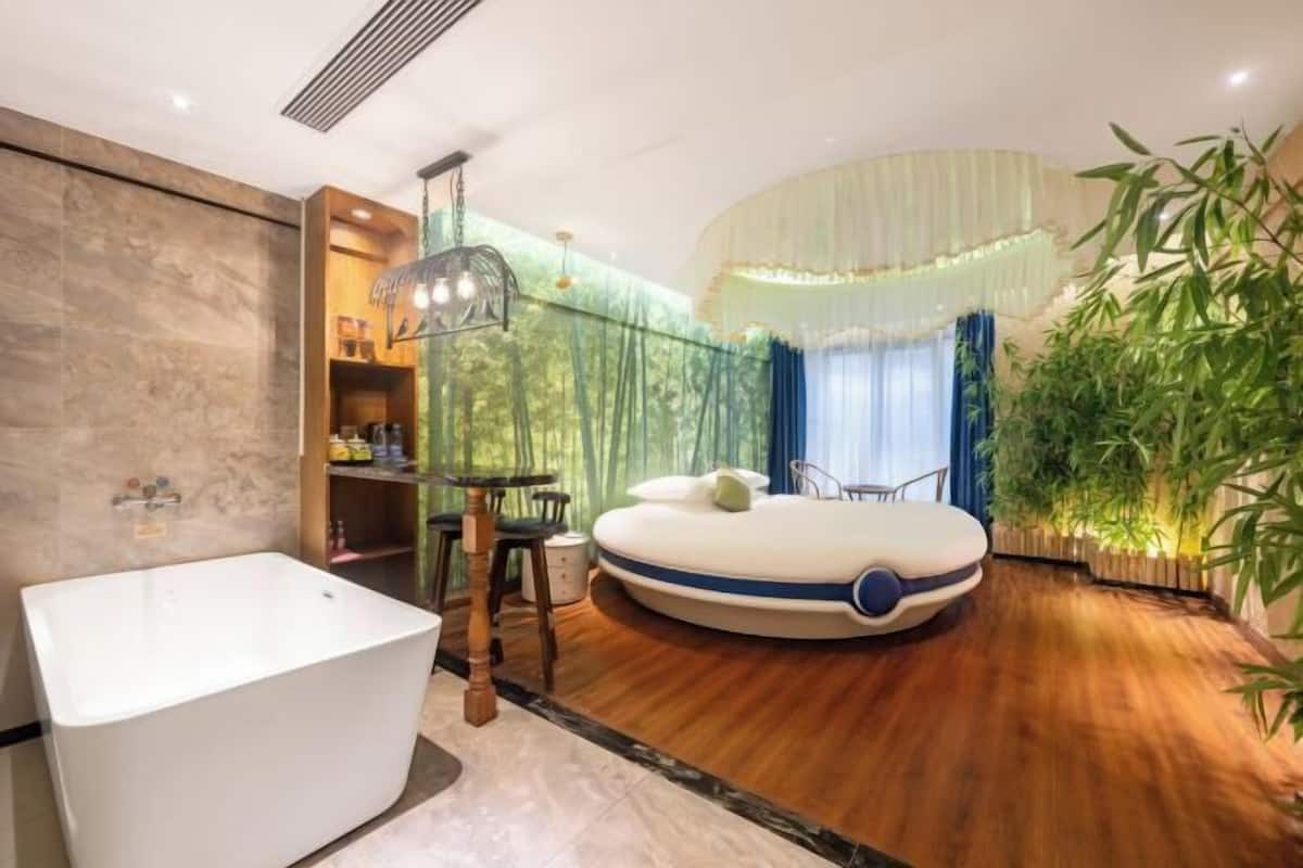 Ein modernes Schlafzimmer mit Badewanne, einem runden Bett, einem Esstisch und einer großen Pflanze.