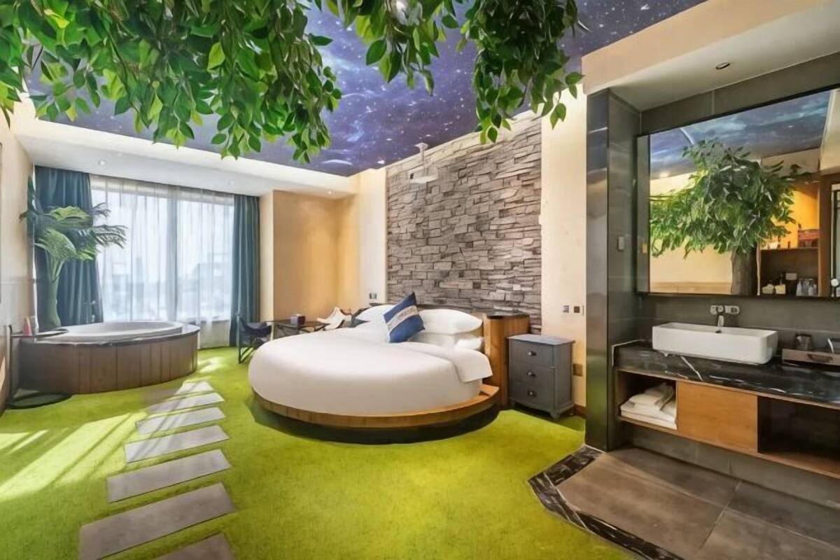 Ein modernes Schlafzimmer mit einem runden Bett, einer Steinwand, einem großen Spiegel und einem grünen Teppich.
