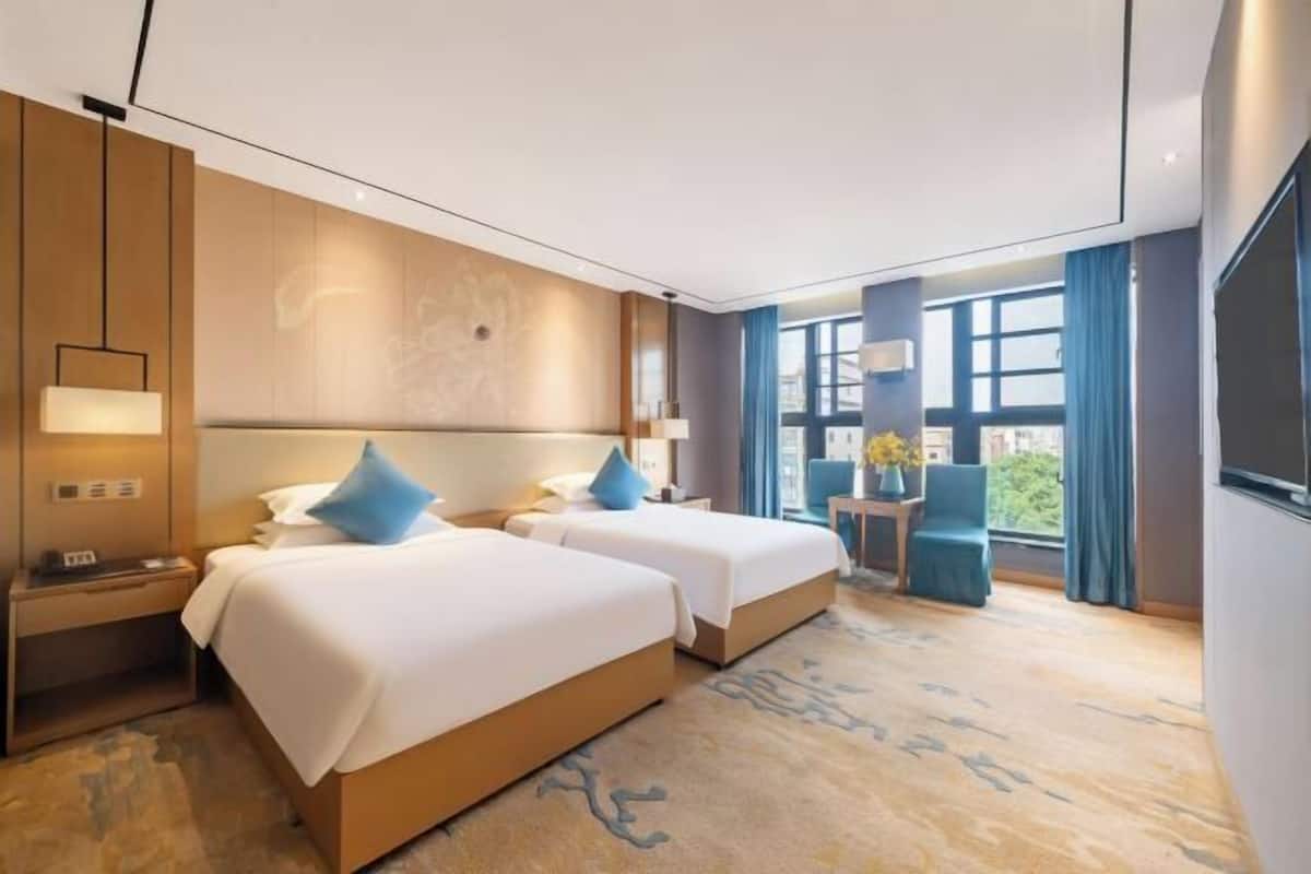 Ein Hotelzimmer mit zwei Betten, einem kleinen Tisch, einem Stuhl und einem Fenster mit Vorhängen.