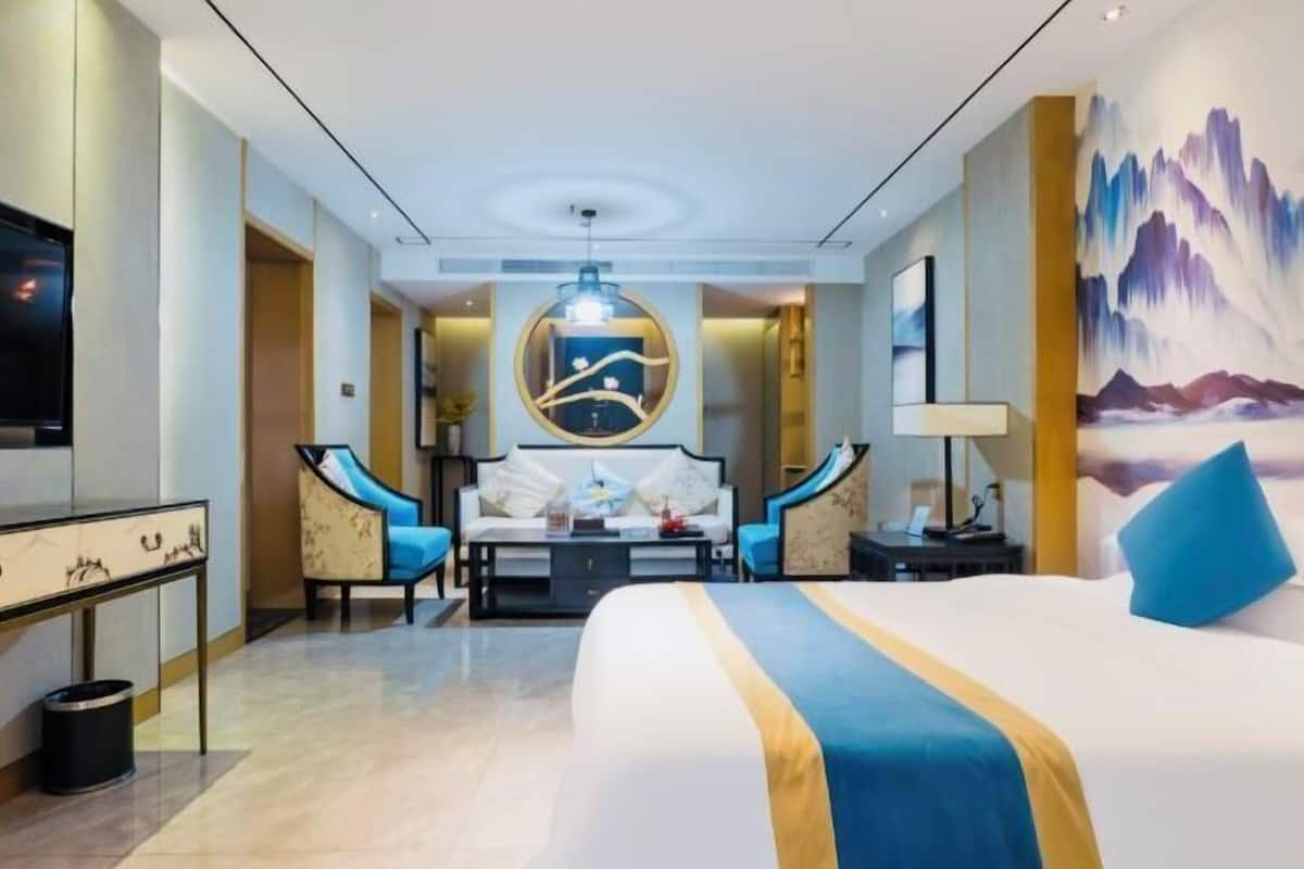 Ein Hotelzimmer mit einem großen Bett, einem Schreibtisch, einem Sessel, einem Sofa, einem Fernseher und einem Bild an der Wand.