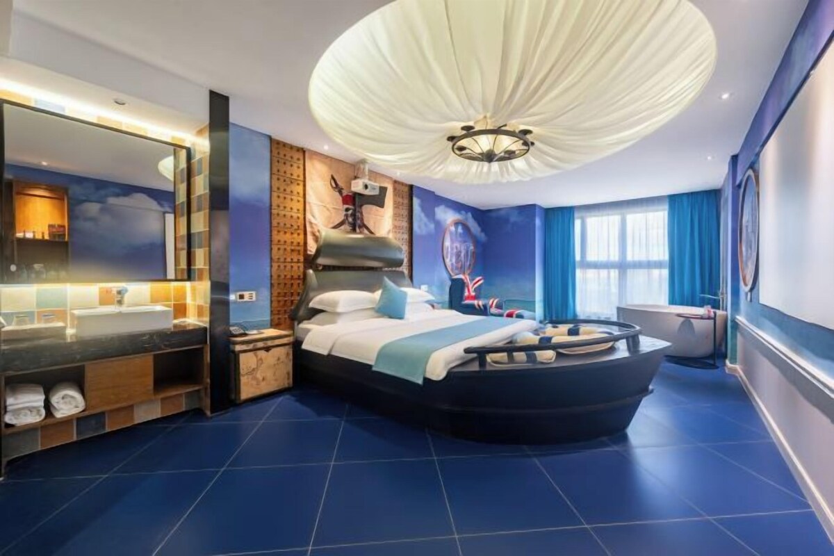 A modern bedroom with a curved bed, a large mirror, a bathtub, and a ceiling light fixture.