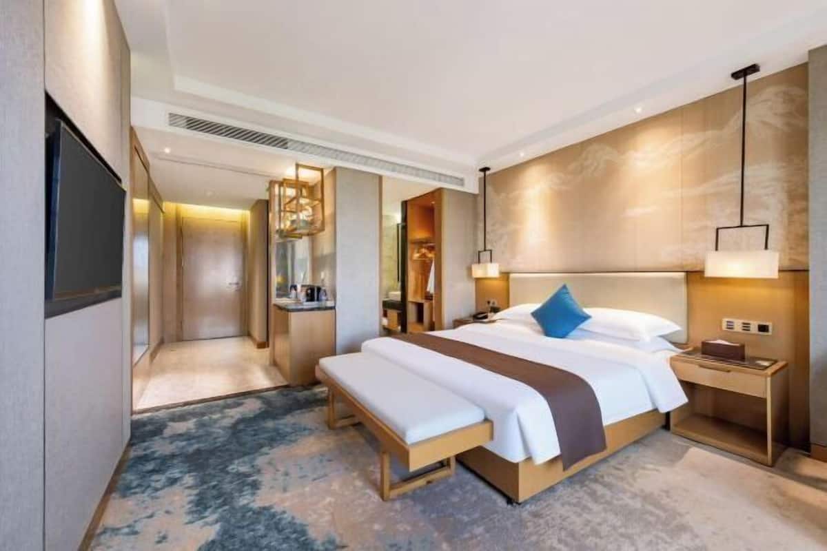 Ein modernes Hotelzimmer mit einem großen Bett, Nachttischen, einer Bank, einem Fernseher und einem durch eine offene Tür einsehbaren Badezimmer.