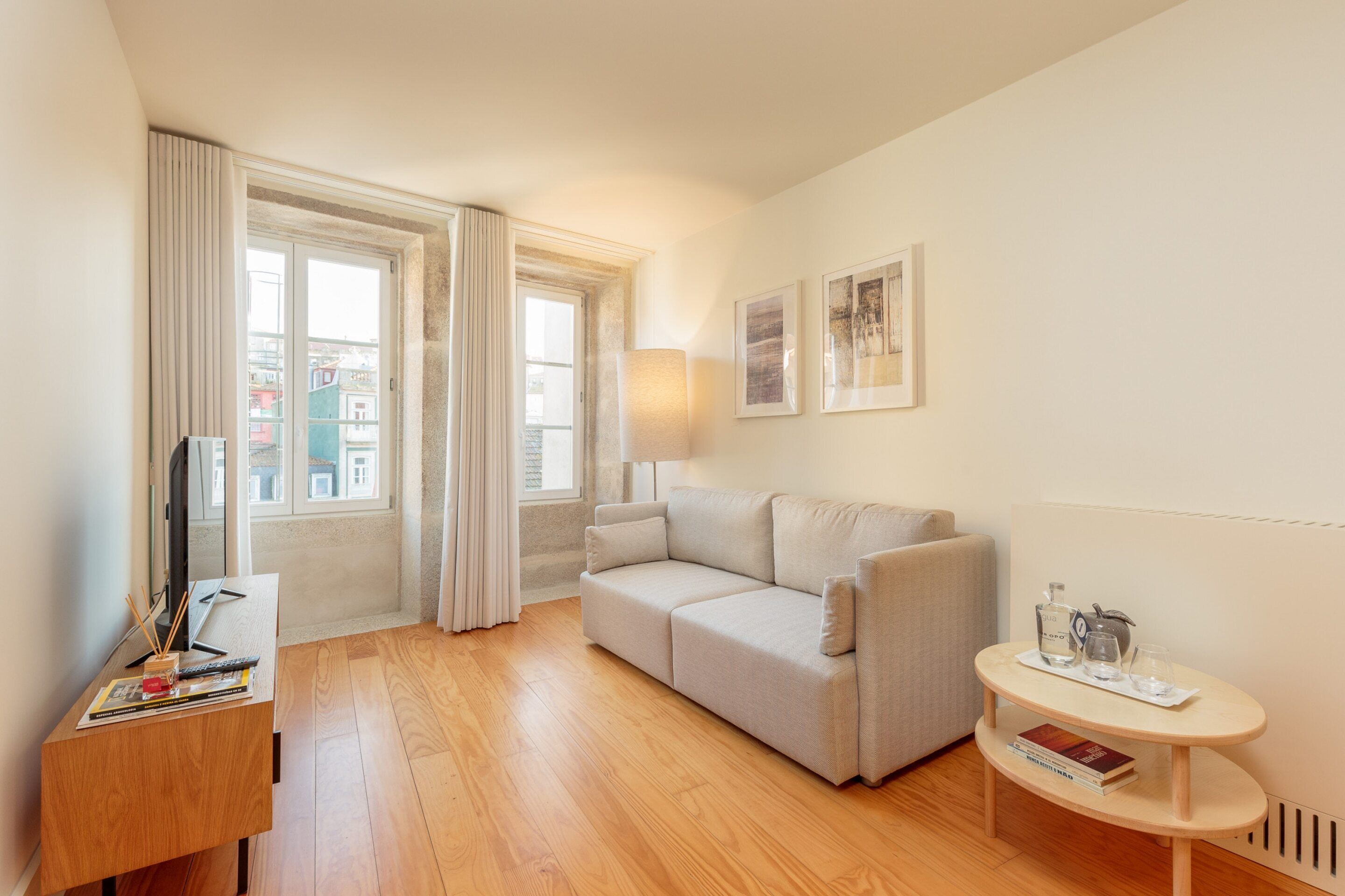 A modern living room with a sofa, a wooden desk, a small round table, and a window with curtains.
