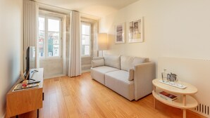 A modern living room with a sofa, a wooden desk, a small round table, and a window with curtains. - Apartment in Porto With Balcony (Porto)
