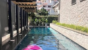 A modern outdoor pool area with a clear pool, a pink inflatable ring, and a stone building in the background. - Air Onia (Budva)