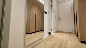 A hallway with wooden flooring and white walls. There are two doors, one with a mirror and the other with a door handle. - Air Onia (Budva)