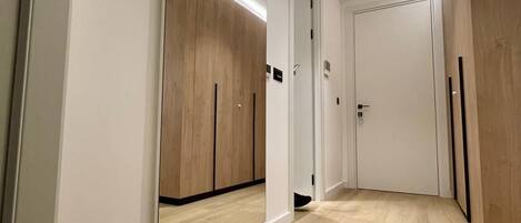A hallway with wooden flooring and white walls. There are two doors, one with a mirror and the other with a door handle.