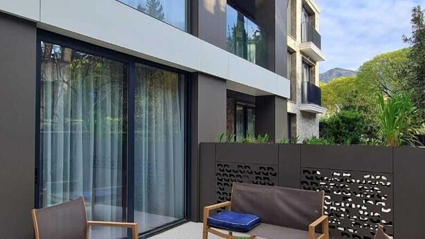 A modern outdoor seating area with a wooden table and chairs, a small potted plant, and a decorative wall panel. - Air Onia (Budva)