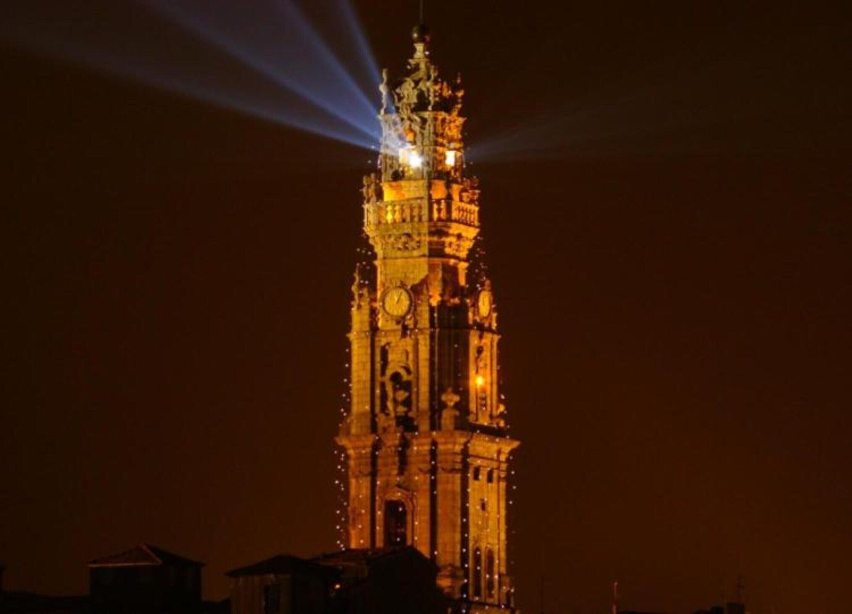 A tower with a clock and illuminated details, surrounded by buildings.