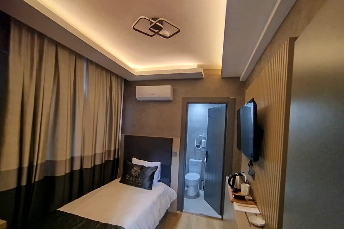 A hotel room with a bed, curtains, a television, a coffee maker, and a bathroom visible through an open door.