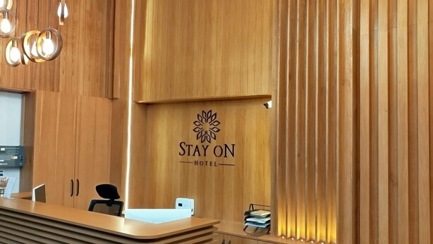 A reception desk with a wooden finish, a logo that reads "STAY ON HOTEL", and a modern light fixture above it. - STAY ON HOTEL (Izmir)