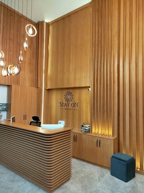 A reception desk with a wooden finish, a logo that reads "STAY ON HOTEL", and a modern light fixture above it. - STAY ON HOTEL (Izmir)