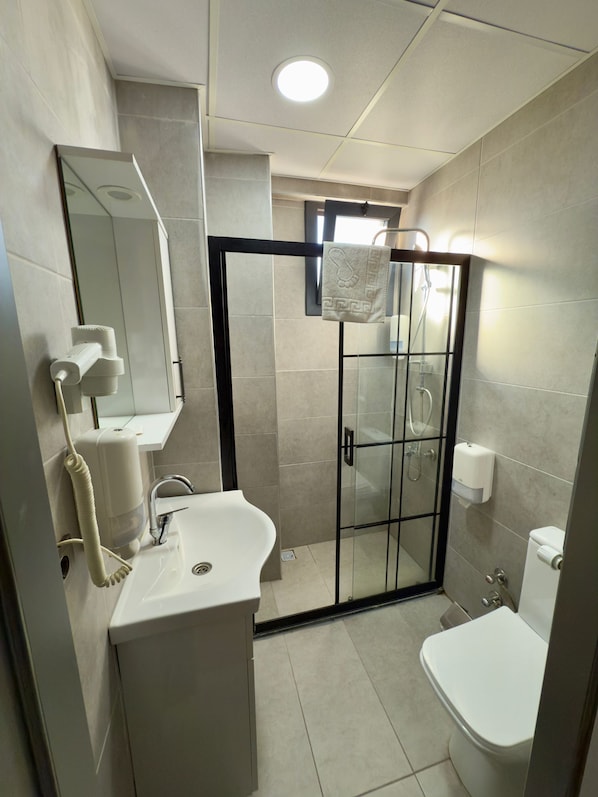 Uma casa de banho moderna com cabine de duche em vidro, lavatório branco, sanita e espelho.