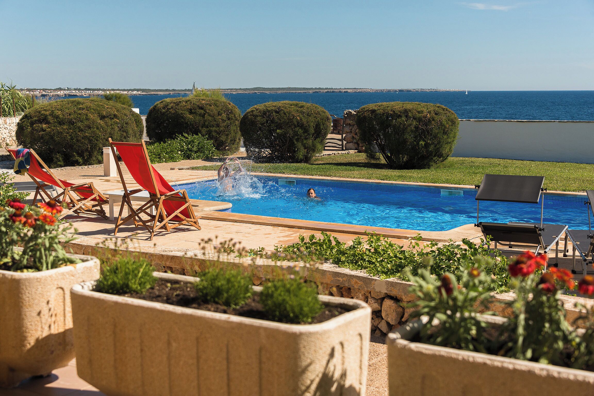 Una piscina amb vistes al mar, envoltada de plantes en testos i gandules.