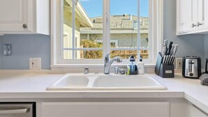 A kitchen with a double sink, a window with a view of neighboring houses, and a countertop with a knife block and a toaster. - @ Marbella Lane - Modern and Sleek Home in Redwood (Redwood City)