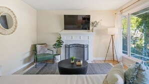 A living room with a fireplace, a television, a green chair, a round table, and a large window. - @ Marbella Lane - Modern and Sleek Home in Redwood (Redwood City)