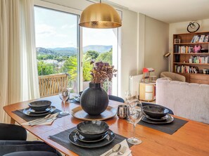 A dining area with a table set for two, a large vase with dried flowers, and a view of the outdoors through a large window. - Villa Riera by Hello Homes Sitges (Sitges)