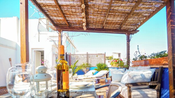 An outdoor dining area with a table set for two, a bottle of wine, and a lounge chair.