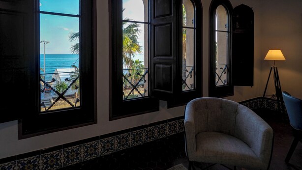 Una habitación con vista al océano a través de ventanales arqueados, una silla y una lámpara.