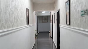 Un couloir étroit et bien éclairé, aux murs blancs et au sol foncé, bordé de tableaux encadrés et d'un panneau de signalisation verte indiquant la sortie.
