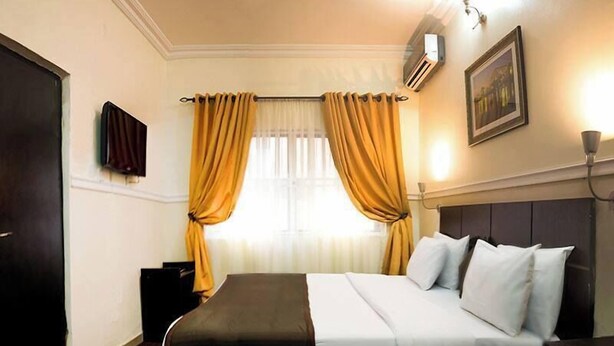 Une chambre d’hôtel équipée d’un lit, d’une table de chevet, d’une télévision, d’une fenêtre avec des rideaux et d’un appareil de climatisation.