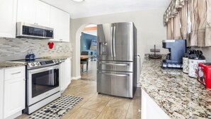 A modern kitchen with stainless steel appliances, white cabinetry, and a checkered floor mat. - Wellington 4BR House (Fort Walton Beach)