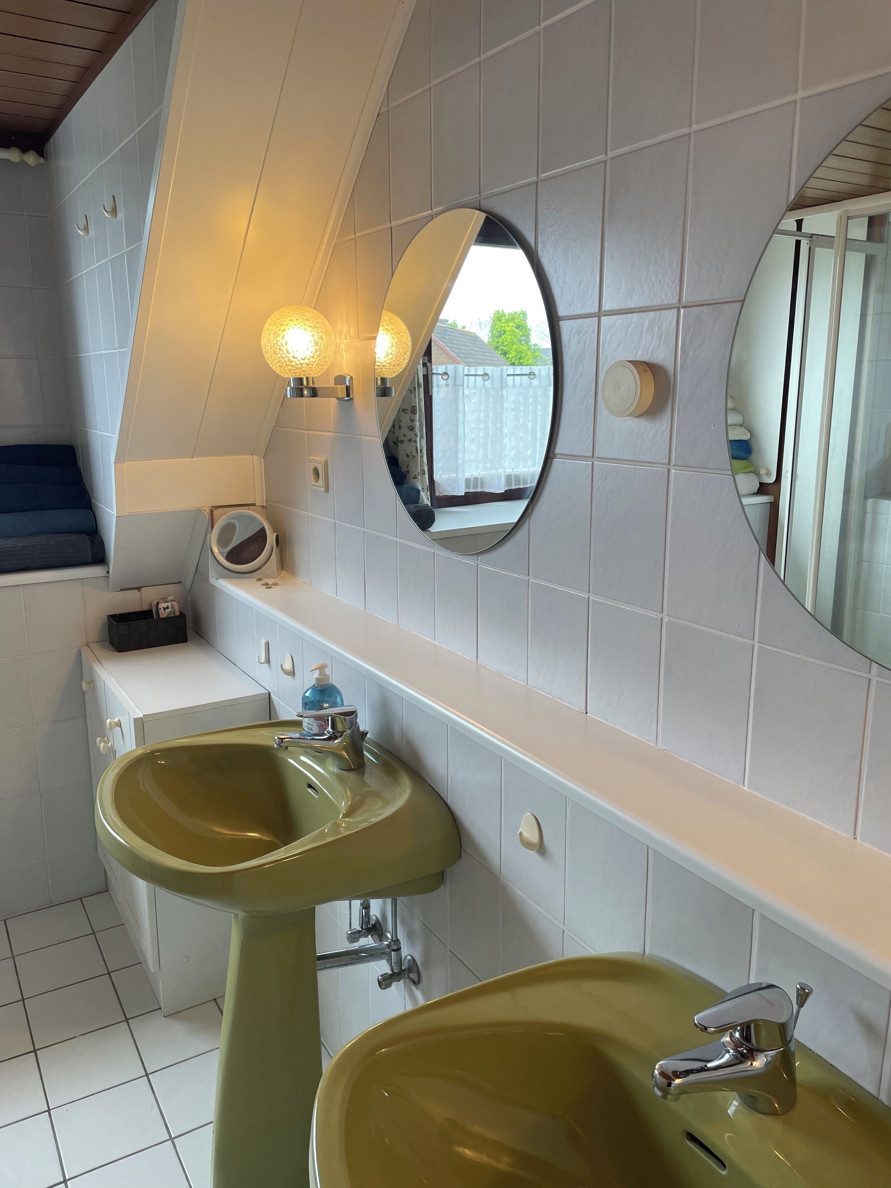 A bathroom with a green sink, a mirror, and a window with curtains.