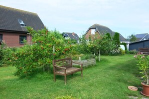 A garden with a wooden bench, fruit trees, and a house with a sloped roof. - Affordable, cozy, standalone vacation home near the seawall, with a patio and garden, and Wi-Fi (Friedrichskoog)