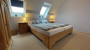 Un dormitorio con una cama de madera, dos mesitas de noche con lámparas, una ventana y un tragaluz.